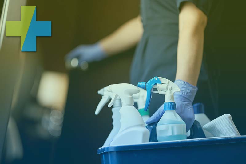 Reinigungskraft mit Schutzhandschuhen und Sprühflaschen im blauen Putzeimer für die Gebäudereinigung